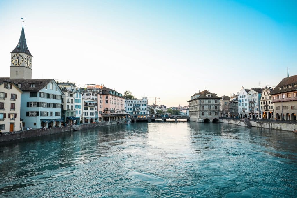 A scenic view of the Zürich riverside featuring a prominent clock tower and historic architecture.