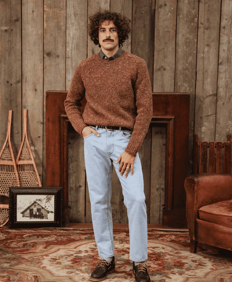 A man in a speckled knit sweater in a rustic wooden interior.