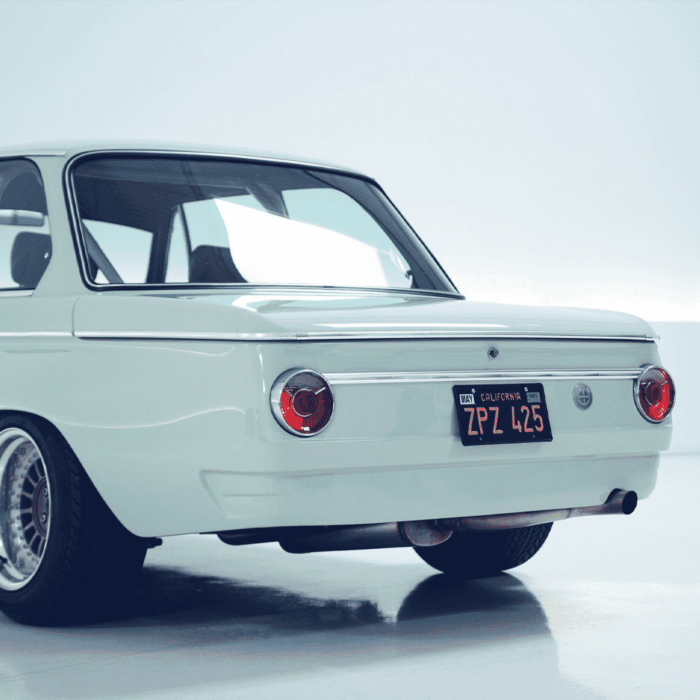 Rear view of a white vintage BMW 2002 showing round taillights and chrome trim.