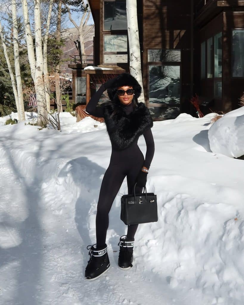 Woman in a black full-body ski suit with a fur-lined hood.