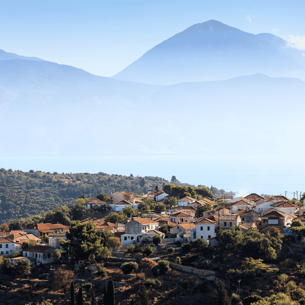 A scenic Mediterranean mountain village with white houses and terracotta roofs under a blue sky.