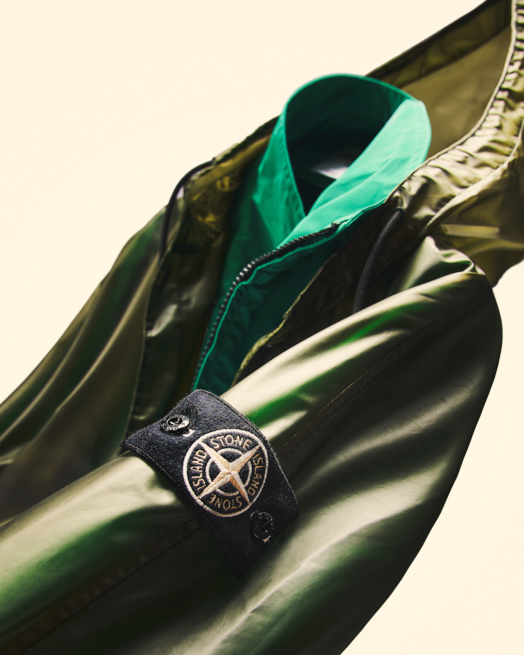 Macro shot of the Stone Island compass patch on the sleeve of the glossy green bomber jacket.