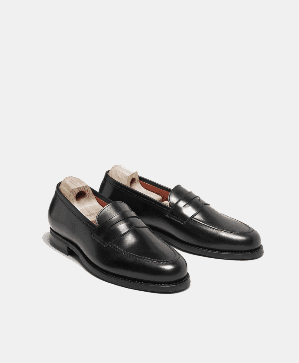A pair of glossy black leather penny loafers with wooden shoe trees.
