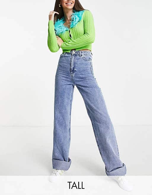 Woman in a lime green ribbed cardigan with turquoise feather trim and wide-leg jeans.