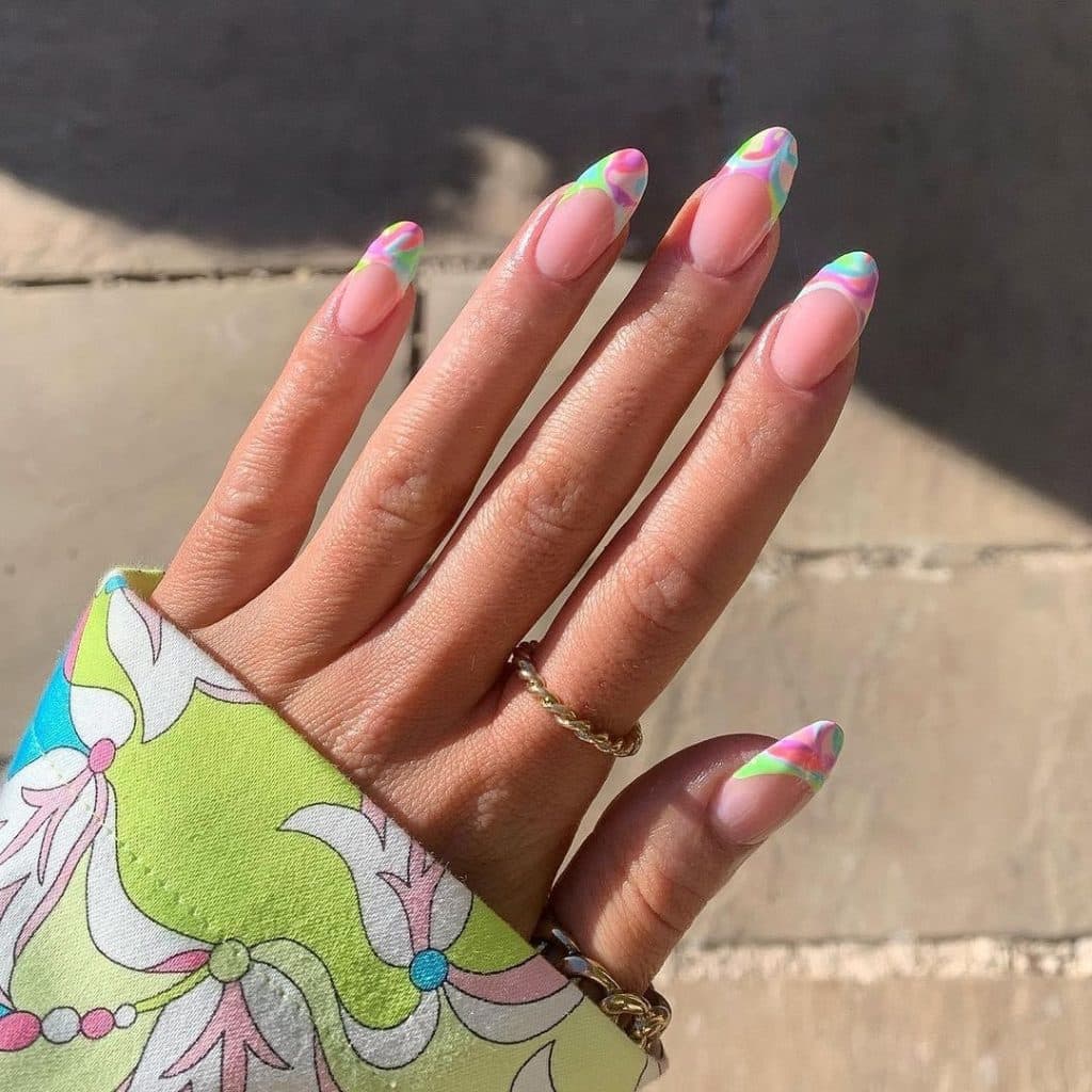 Hand with pastel rainbow marble nail art and gold rings.