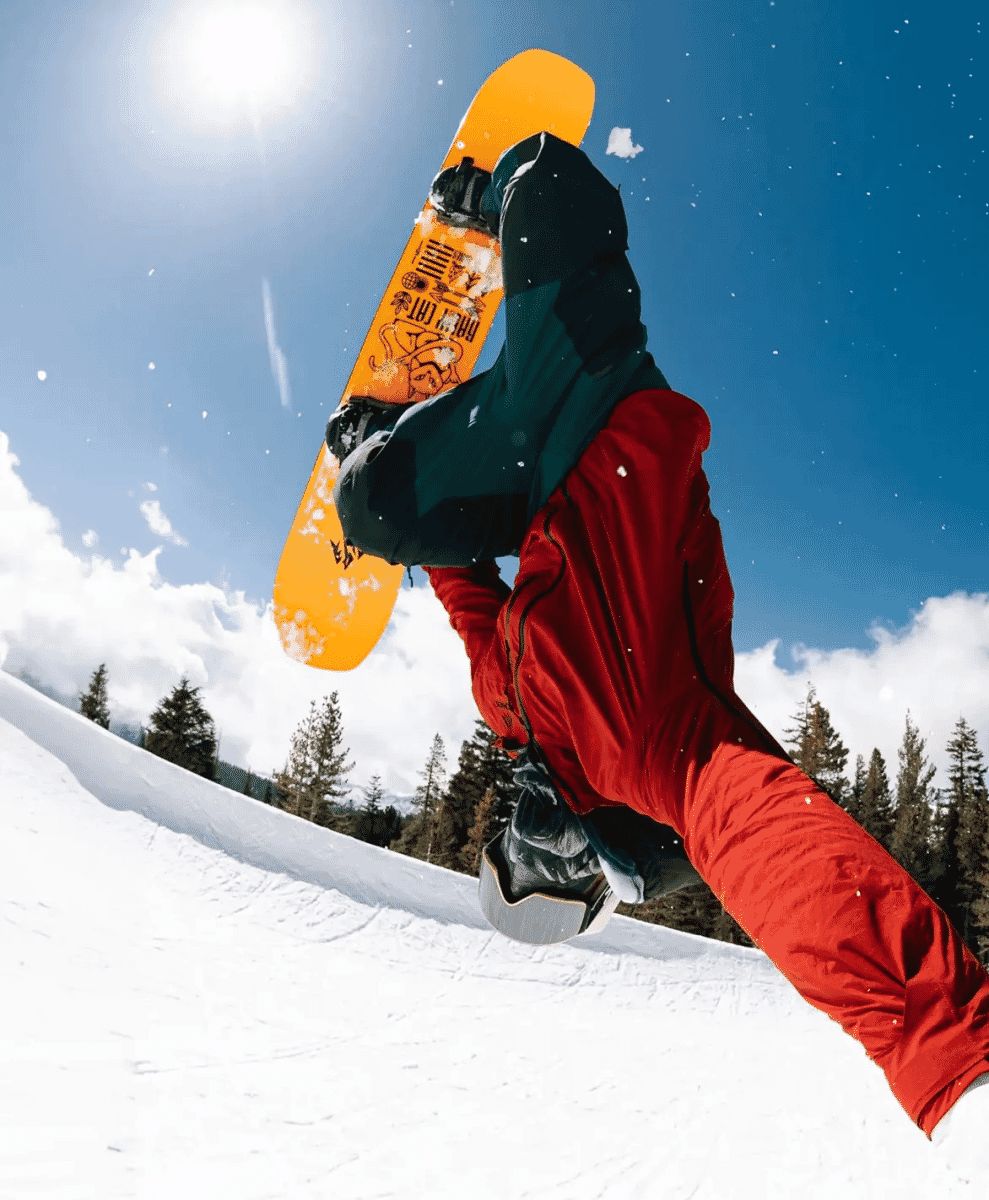 A snowboarder in a red jacket performing a mid-air grab against a bright blue sky.