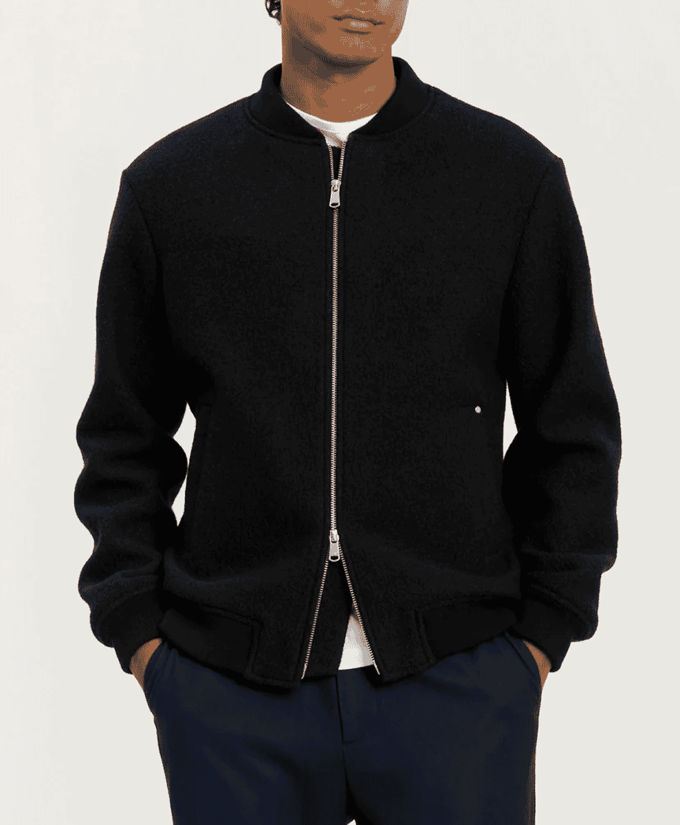 Studio shot of a black wool bomber jacket with a silver zipper and dark trousers.