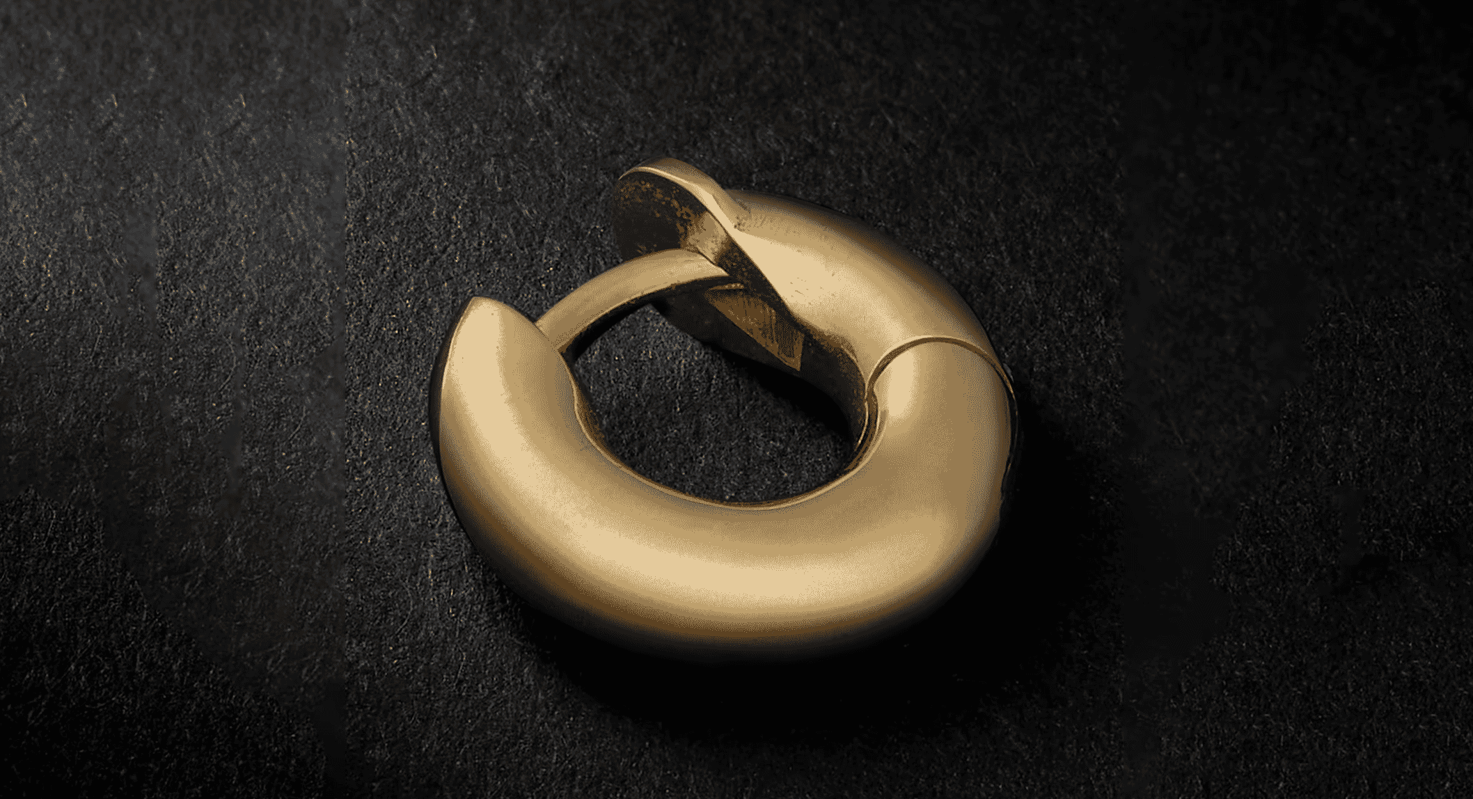 Close-up of a textured gold hoop earring on a dark background showing intricate metallic details.