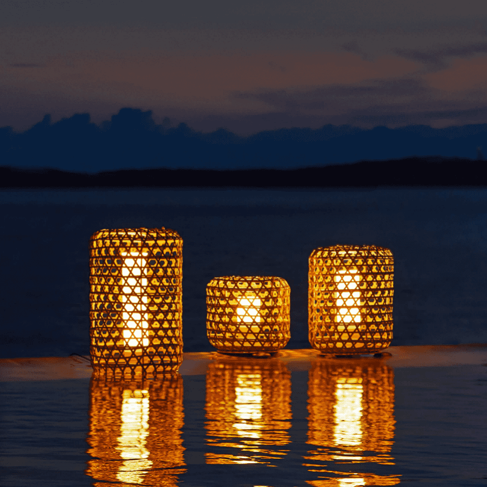 Woven bamboo lanterns with warm light reflecting in a swimming pool at dusk.