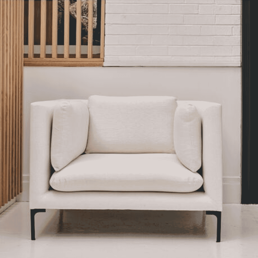 A modern white upholstered armchair against a white brick wall and wooden panels.