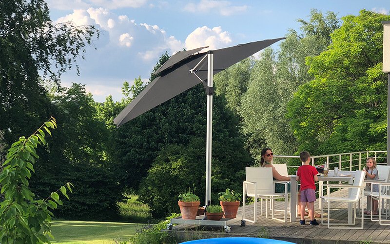 A woman and two children sitting on a wooden deck in the shade of a large patio umbrella.