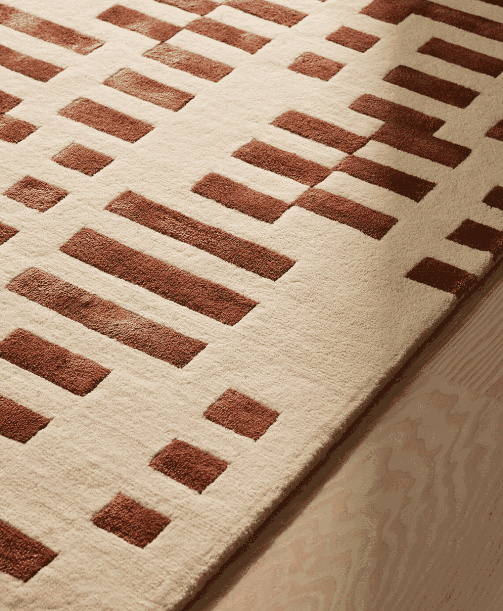 Close-up of a cream-colored rug with brown geometric rectangular patterns on a wooden floor.
