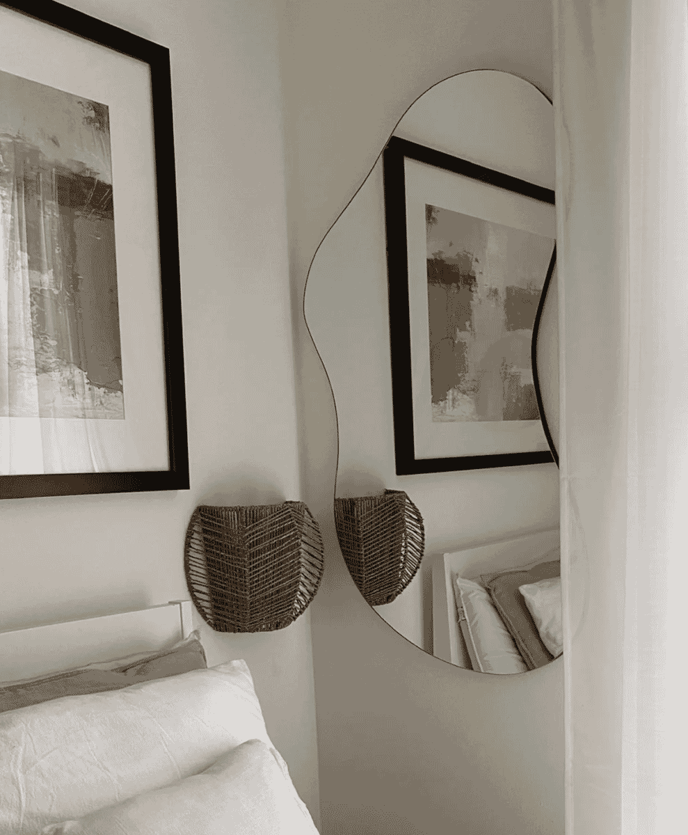 Modern bedroom corner with a wavy-edged mirror and abstract black-framed art.