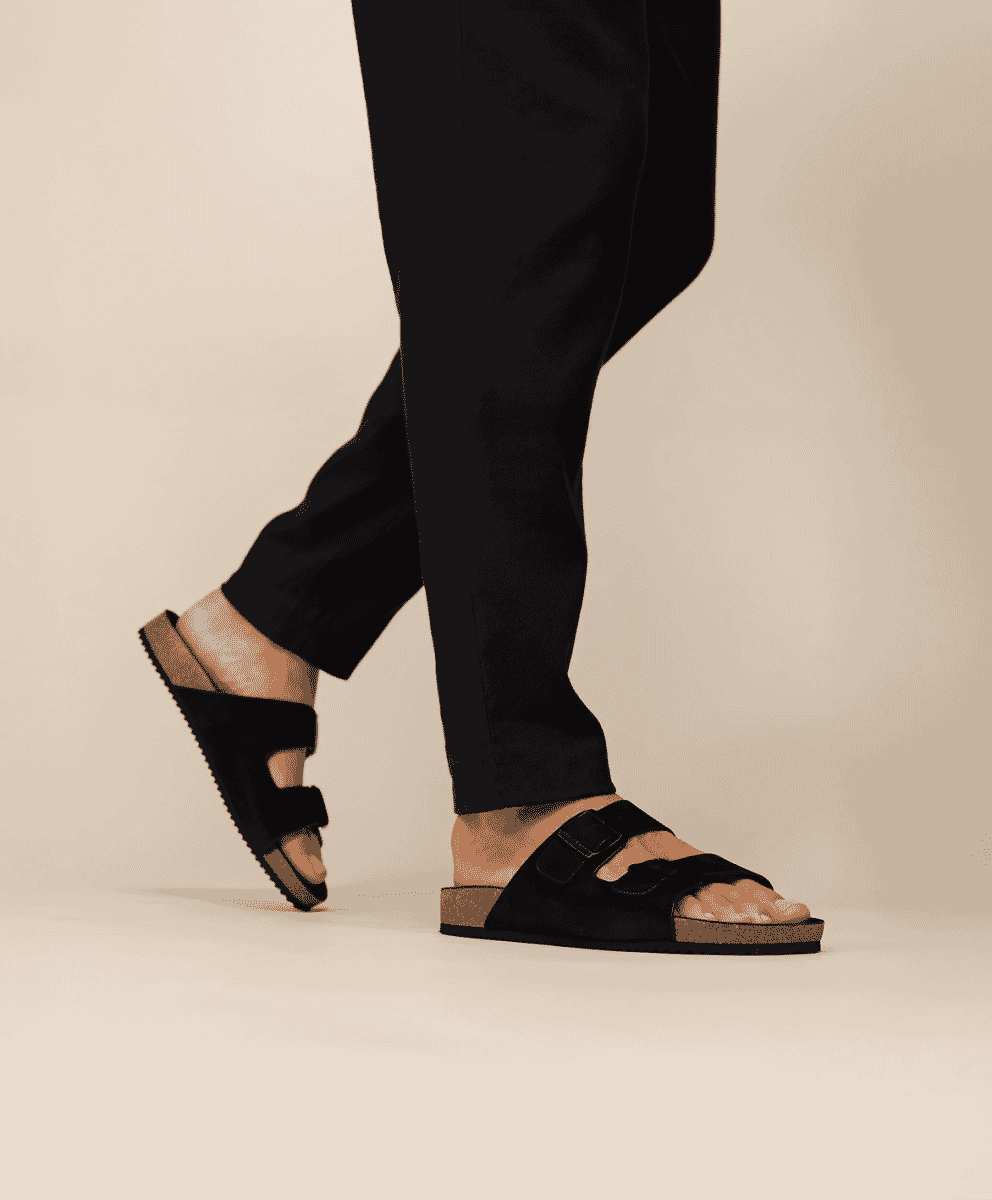 A person wearing black suede double-strap sandals with cork soles.