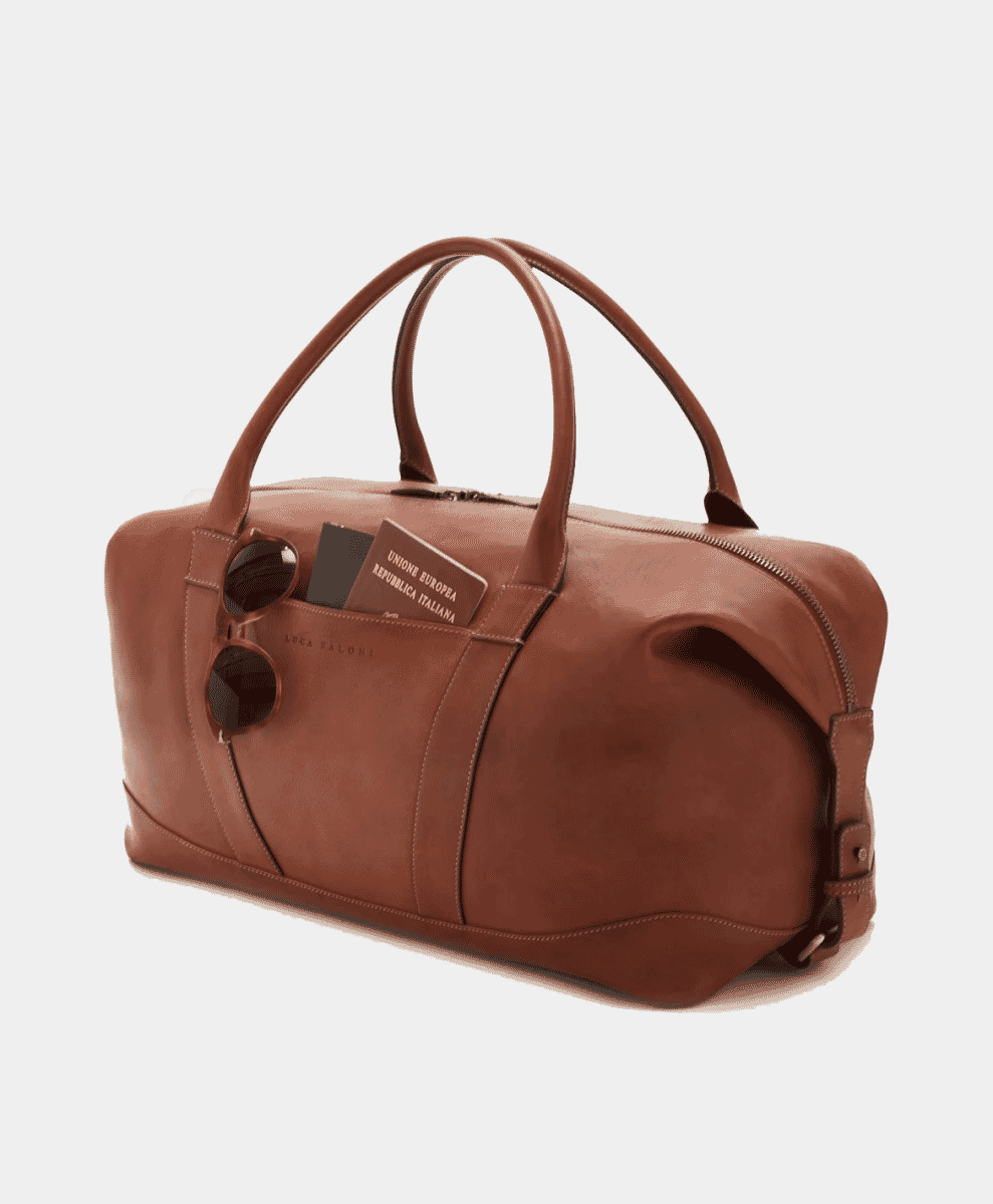 Brown leather duffel bag with a front pocket containing sunglasses and an Italian passport.