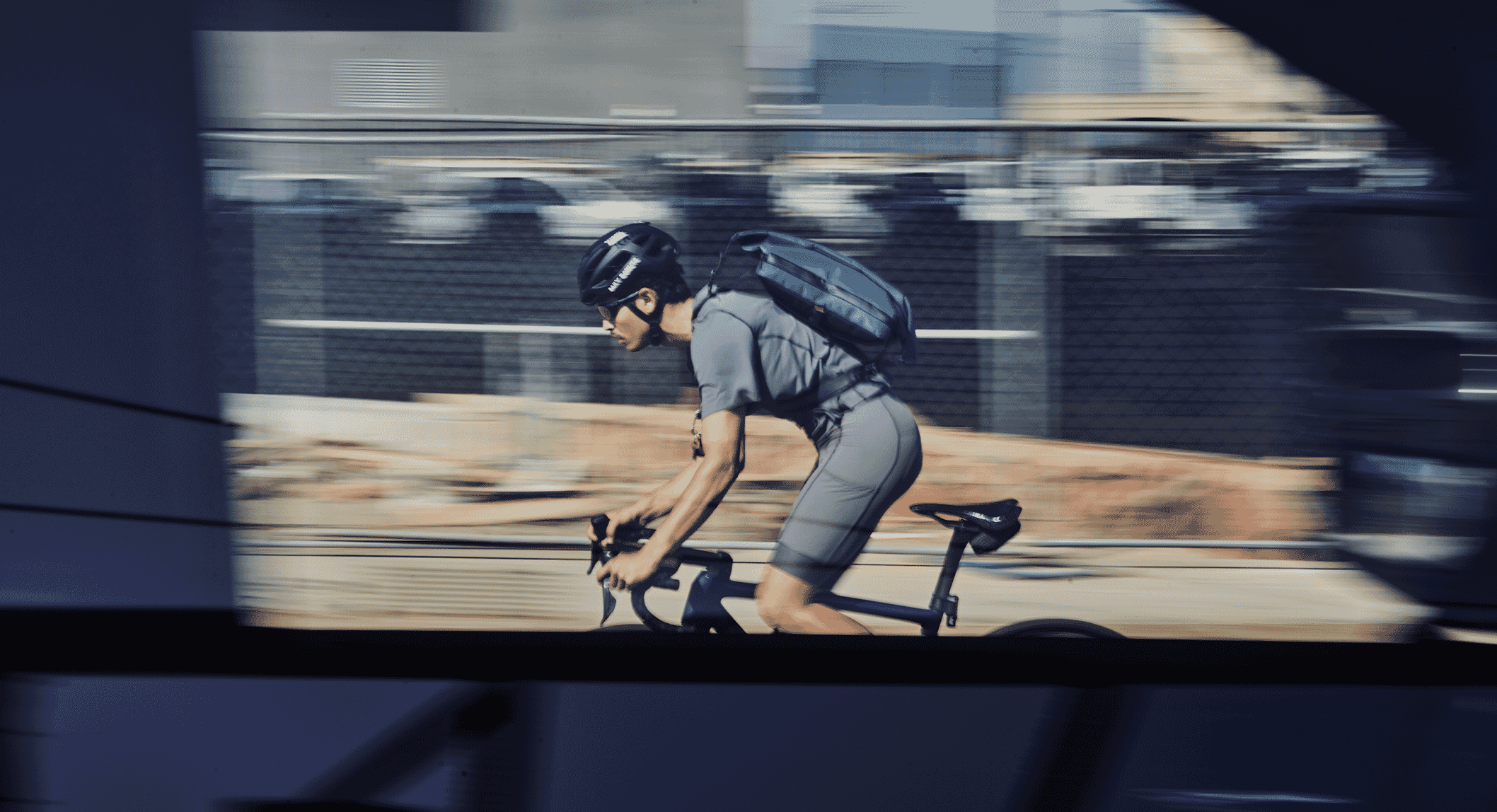 A cyclist in motion with a backpack, blurred against an urban background to convey speed.