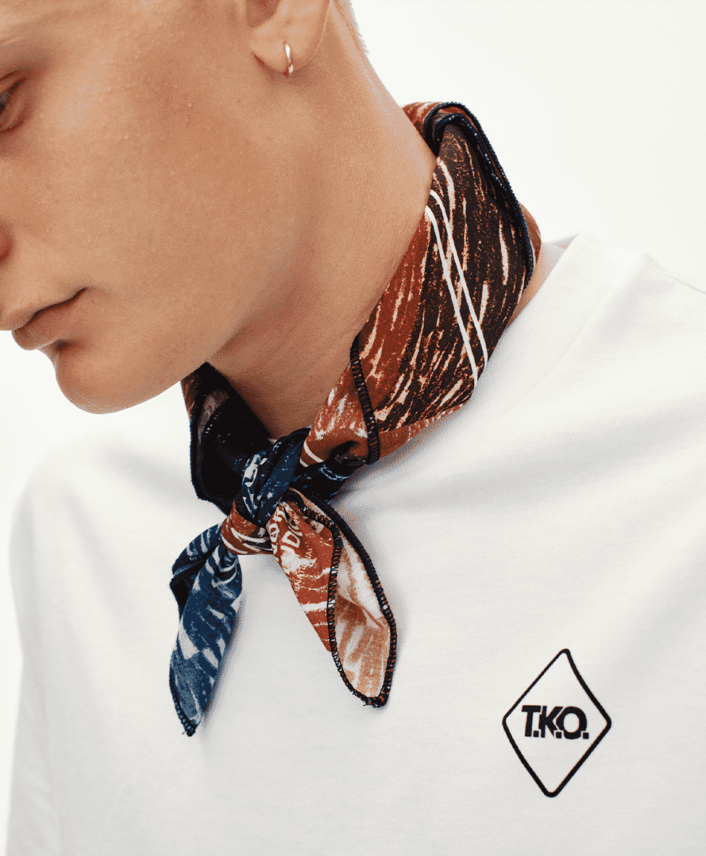 Close-up of a white T-shirt with diamond-shaped T.K.O. logo and a patterned neck scarf.