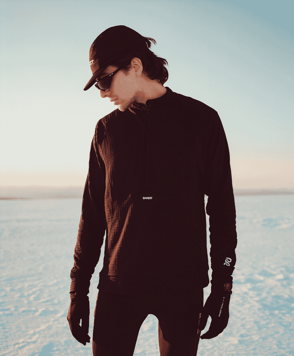 A man in a black Bandit quarter-zip pullover standing in a snowy landscape.