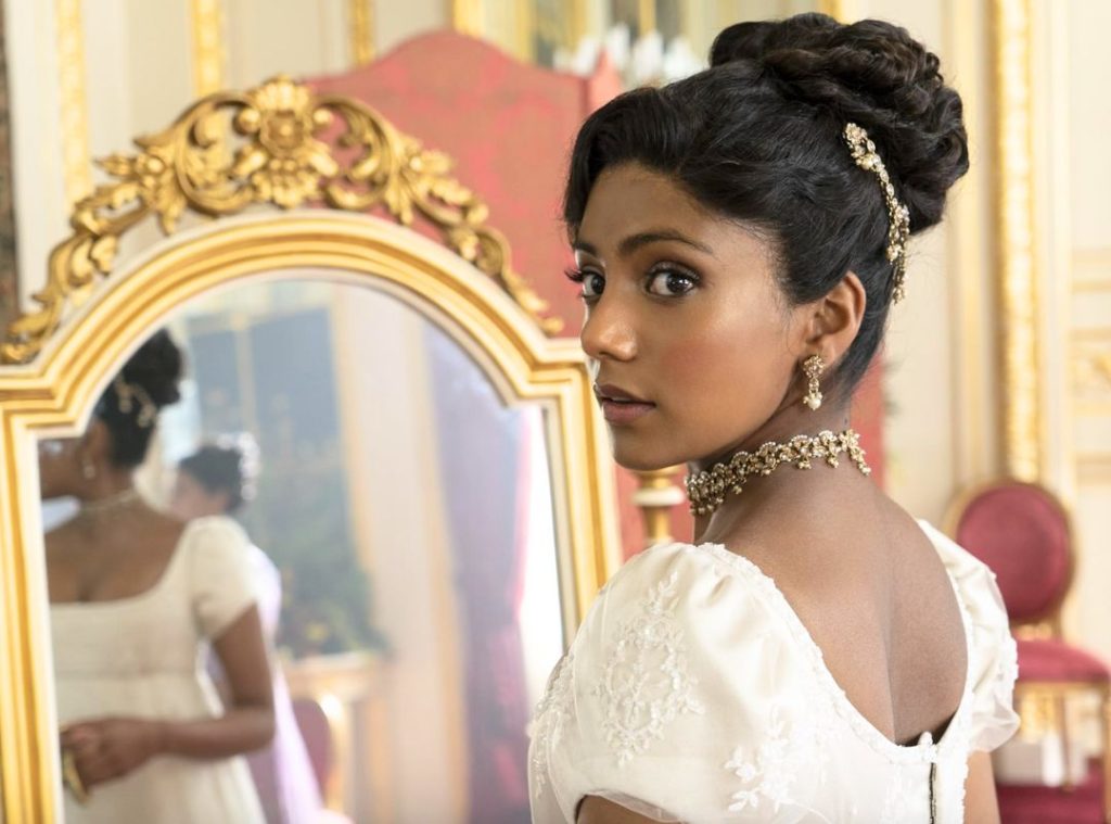 Penelope Featherington peering through a doorway holding a quill