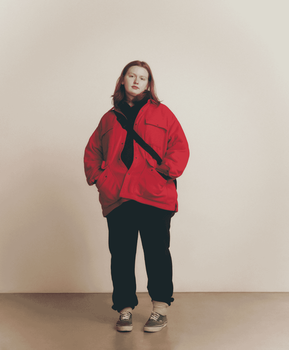 Person with red hair wearing a bold red oversized jacket and black turtleneck.