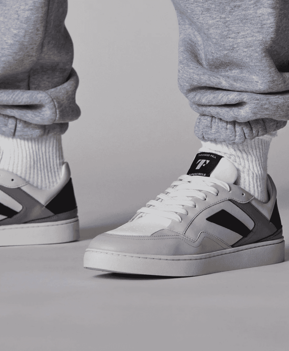 Close-up of Thousand Fell Supercircle sneakers paired with grey sweatpants and white socks.