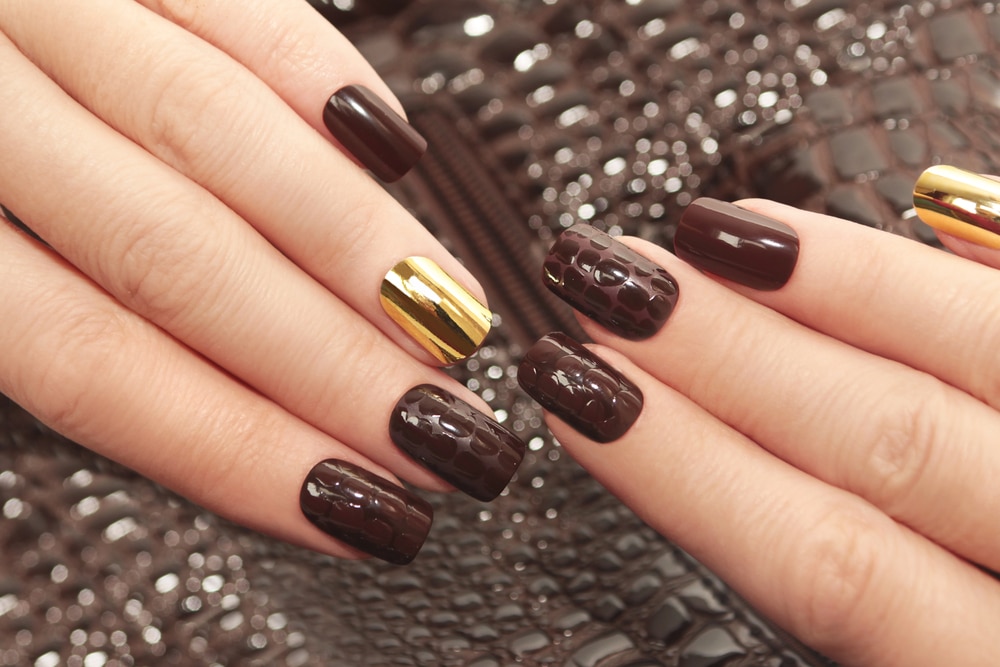 Brown nail art featuring gold foil accents and textured patterns against a brown background.