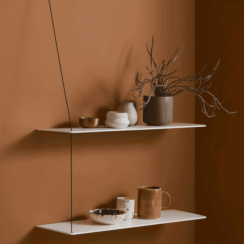 White floating shelves against a brown wall featuring ceramic pots and dried botanical decor.
