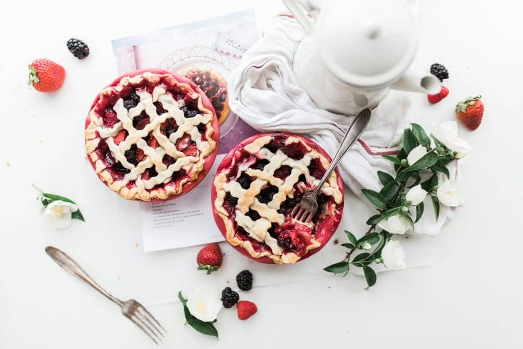 Rustic berry lattice pies on a table with a floral tea set and fresh berries.