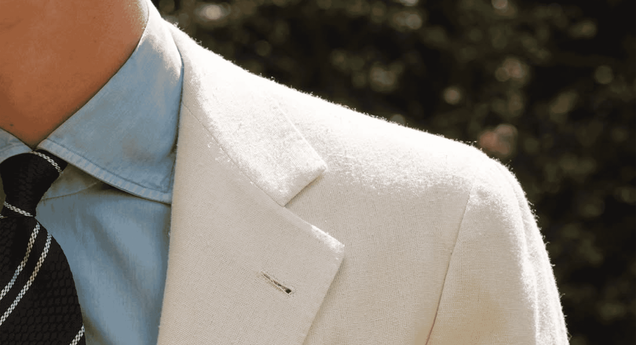 Man wearing a light-colored textured blazer over a light blue shirt and patterned tie.