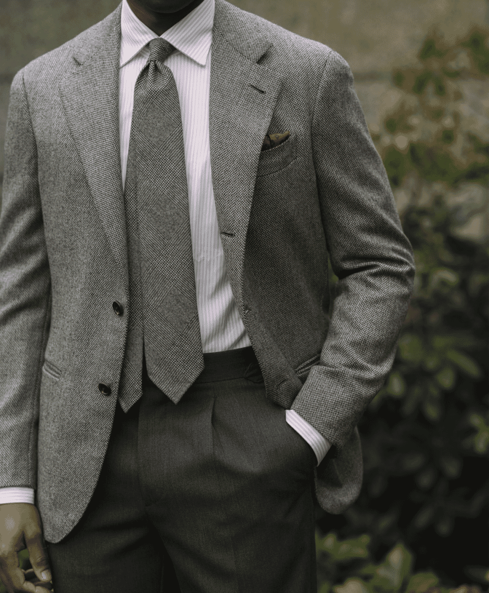 A man in a textured grey tweed blazer with a striped shirt and tie.
