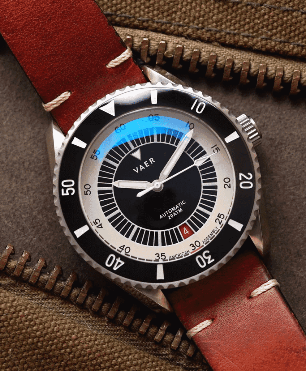 Vaer dive watch with a red leather strap resting on textured brown utility fabric.