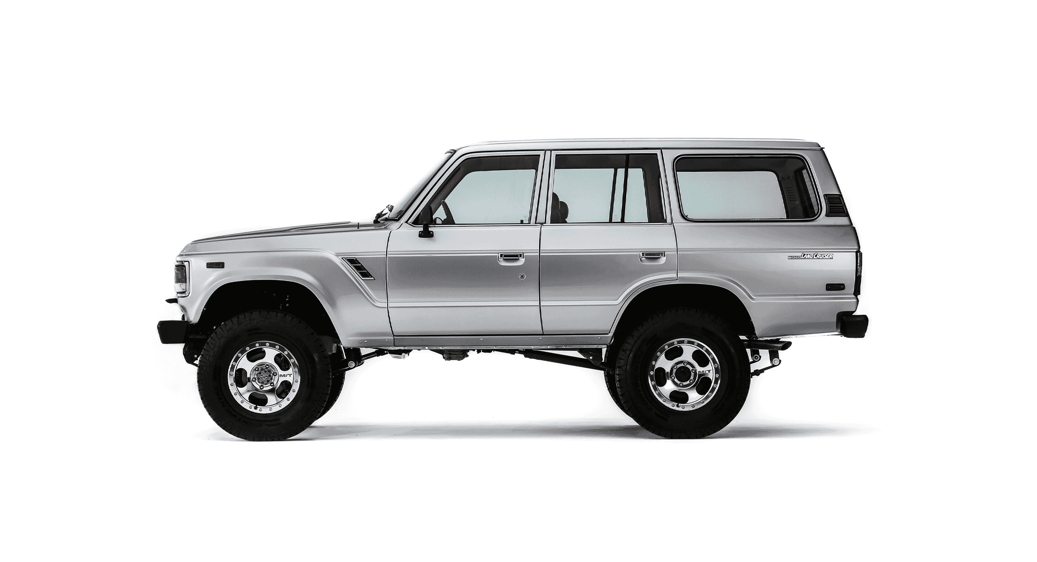 Silver Toyota Land Cruiser SUV in side profile view, featuring lifted suspension and custom wheels.