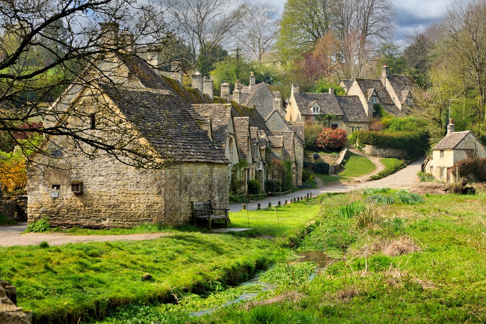 English village scene with historic thatched-roof cottages and a small stream.