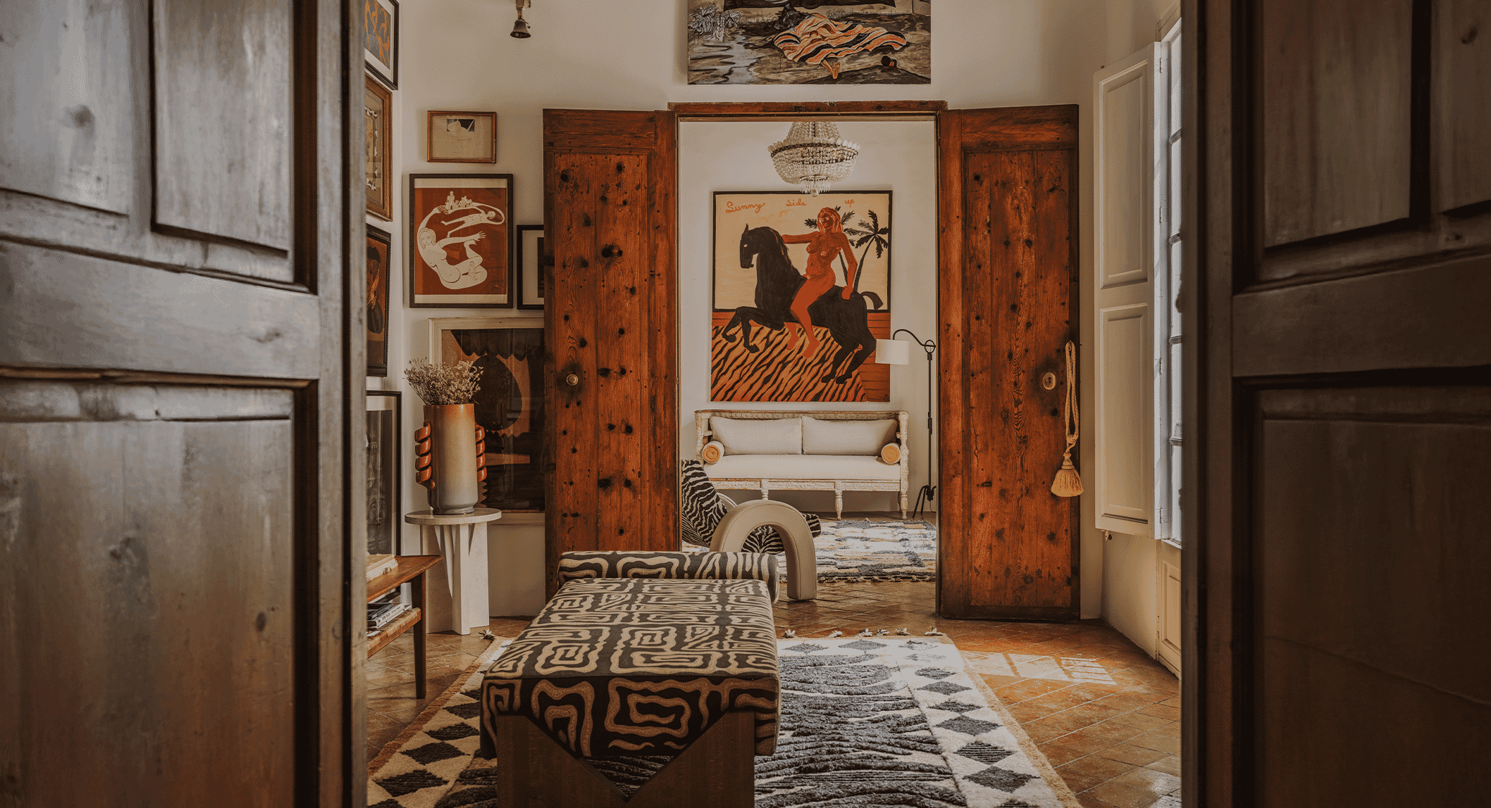Warmly lit interior hallway with rustic wooden doors, eclectic wall art, and patterned rugs.