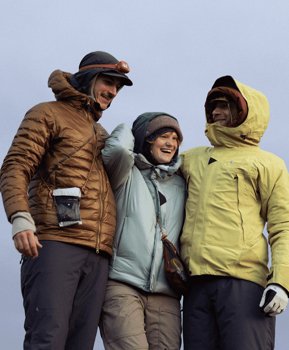 Three people laughing in vibrant technical jackets and mountaineering gear.