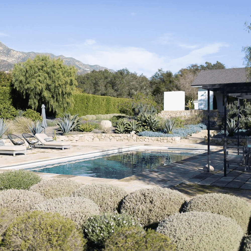 A serene outdoor poolside scene with lounge chairs, stone pathways, and a mountain backdrop.