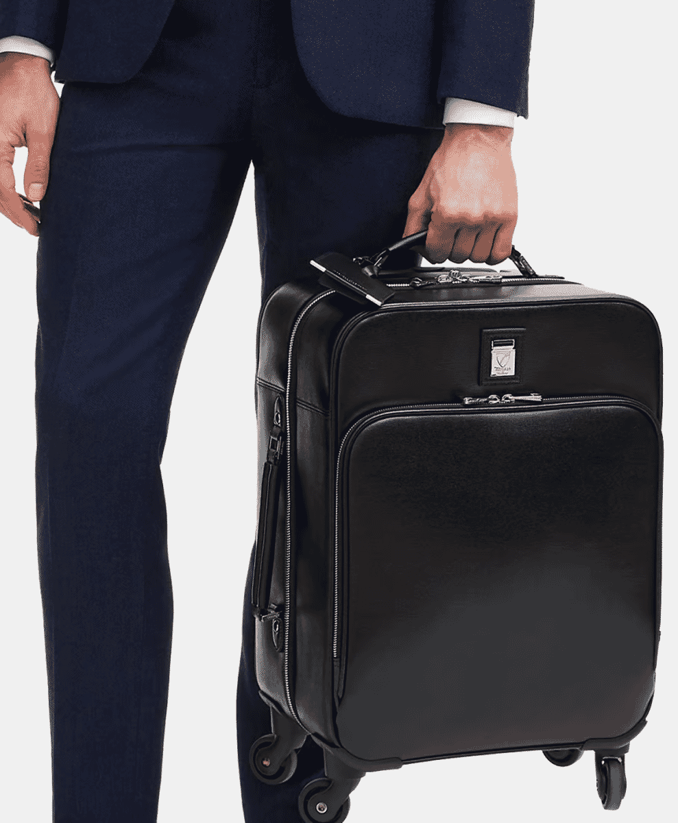 Man in a navy suit pulling a black leather rolling cabin bag with dual wheels.