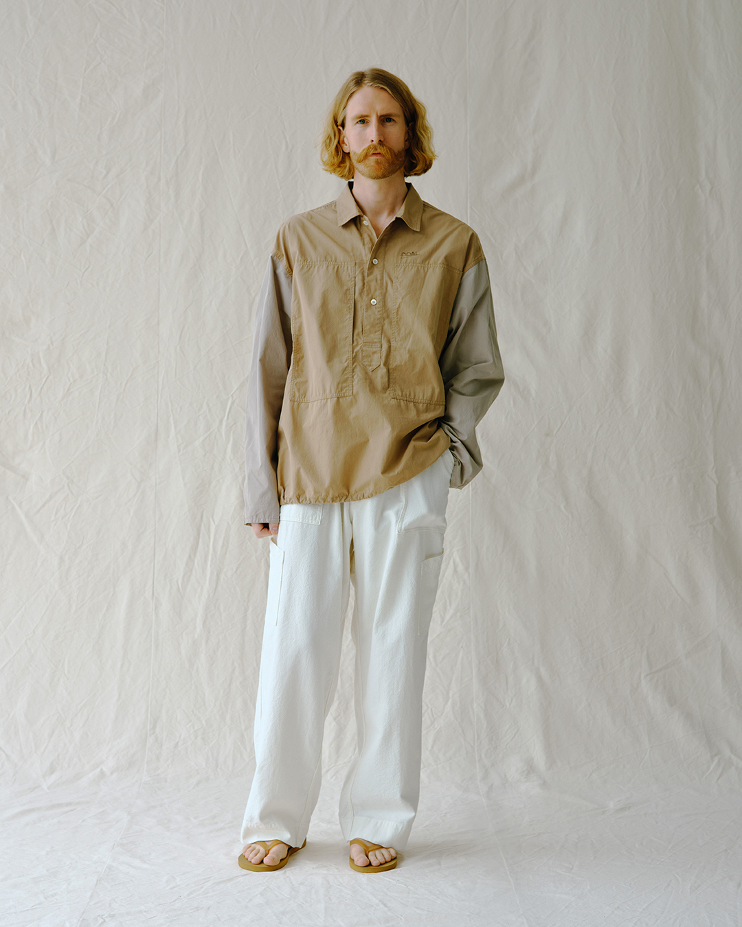 Model in a beige and gray color-blocked utility shirt with wide-leg white pants.