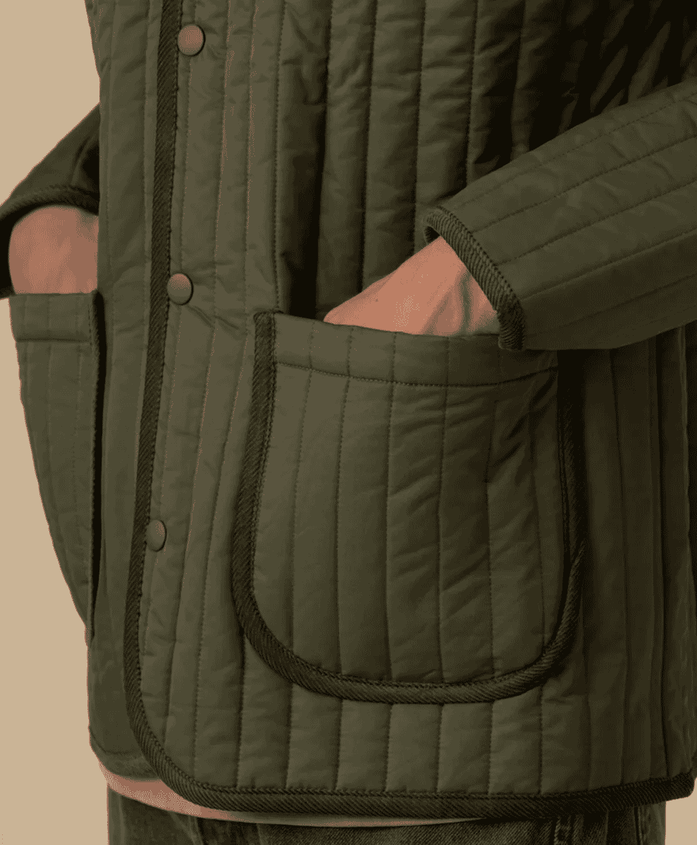 Close-up detail of an olive green quilted jacket with vertical stitching.