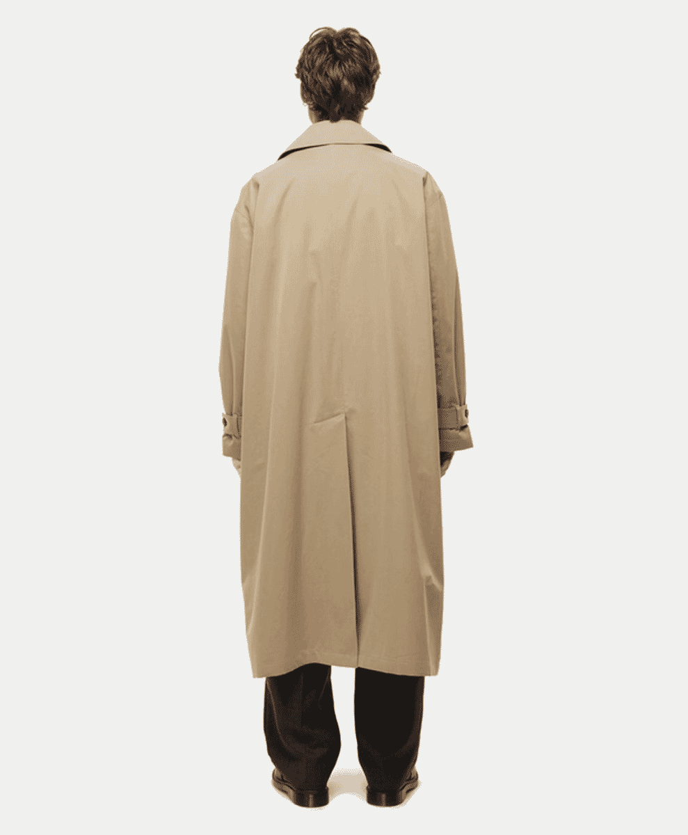 Rear view of a man in a long beige tailored trench coat with wide lapels.