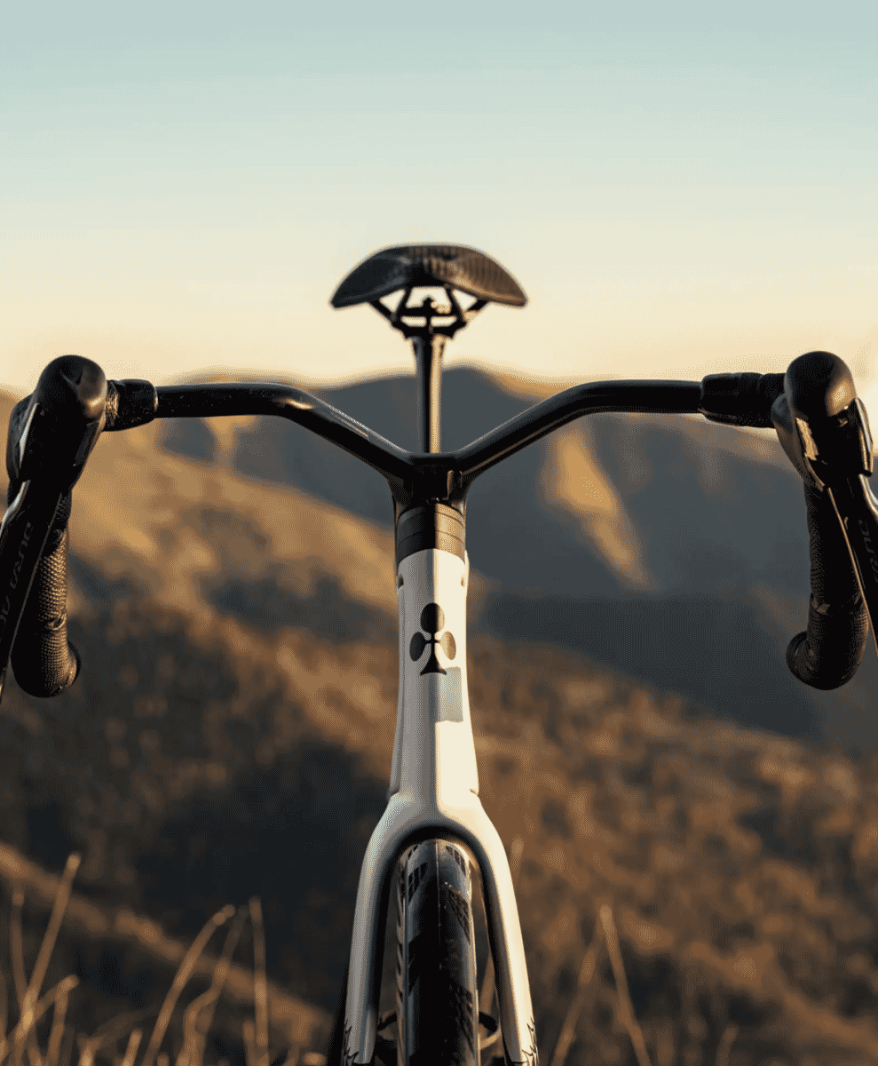Front view of a white frame road bike with black handlebars against a golden-hour mountain backdrop.