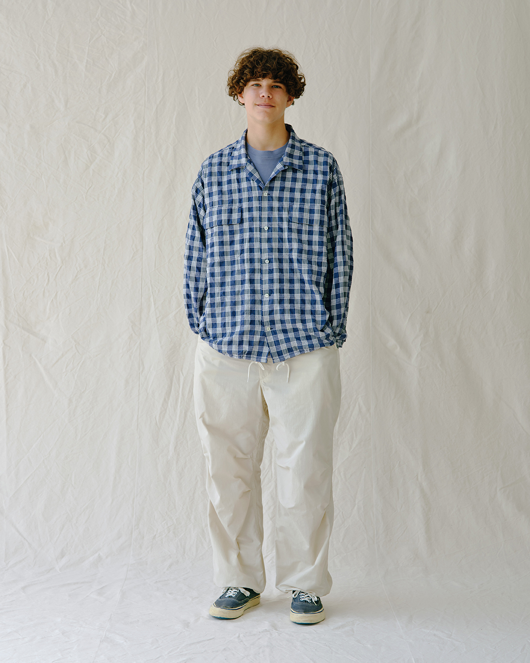 Full body shot of a model in an oversized plaid shirt and loose off-white pants.