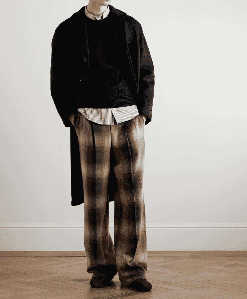 A man wearing wide-leg pleated checked wool flannel trousers with a black coat.