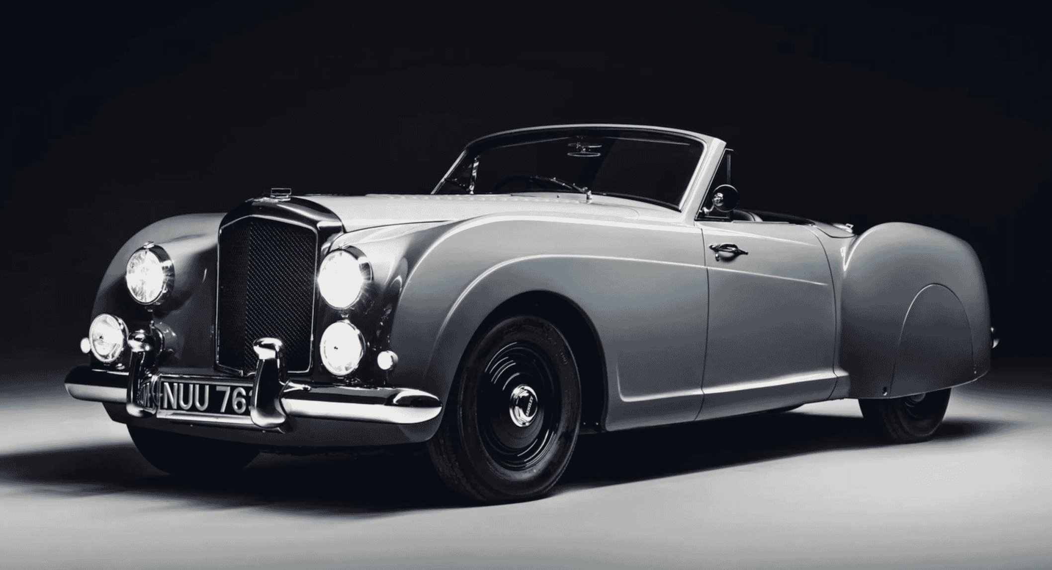 Vintage silver Bentley convertible with chrome accents and round headlights.