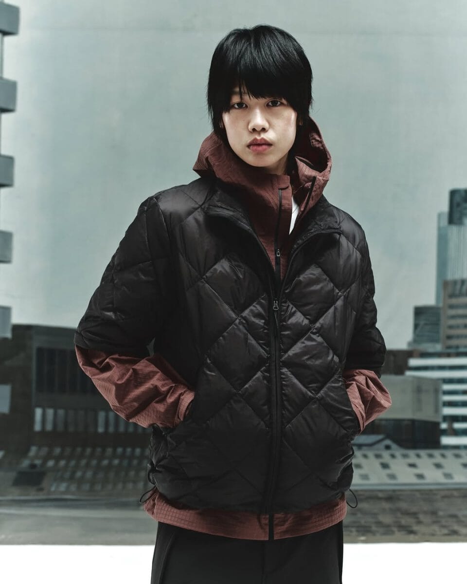 A person wearing a black diamond-quilted puffer jacket over a maroon hooded layer.