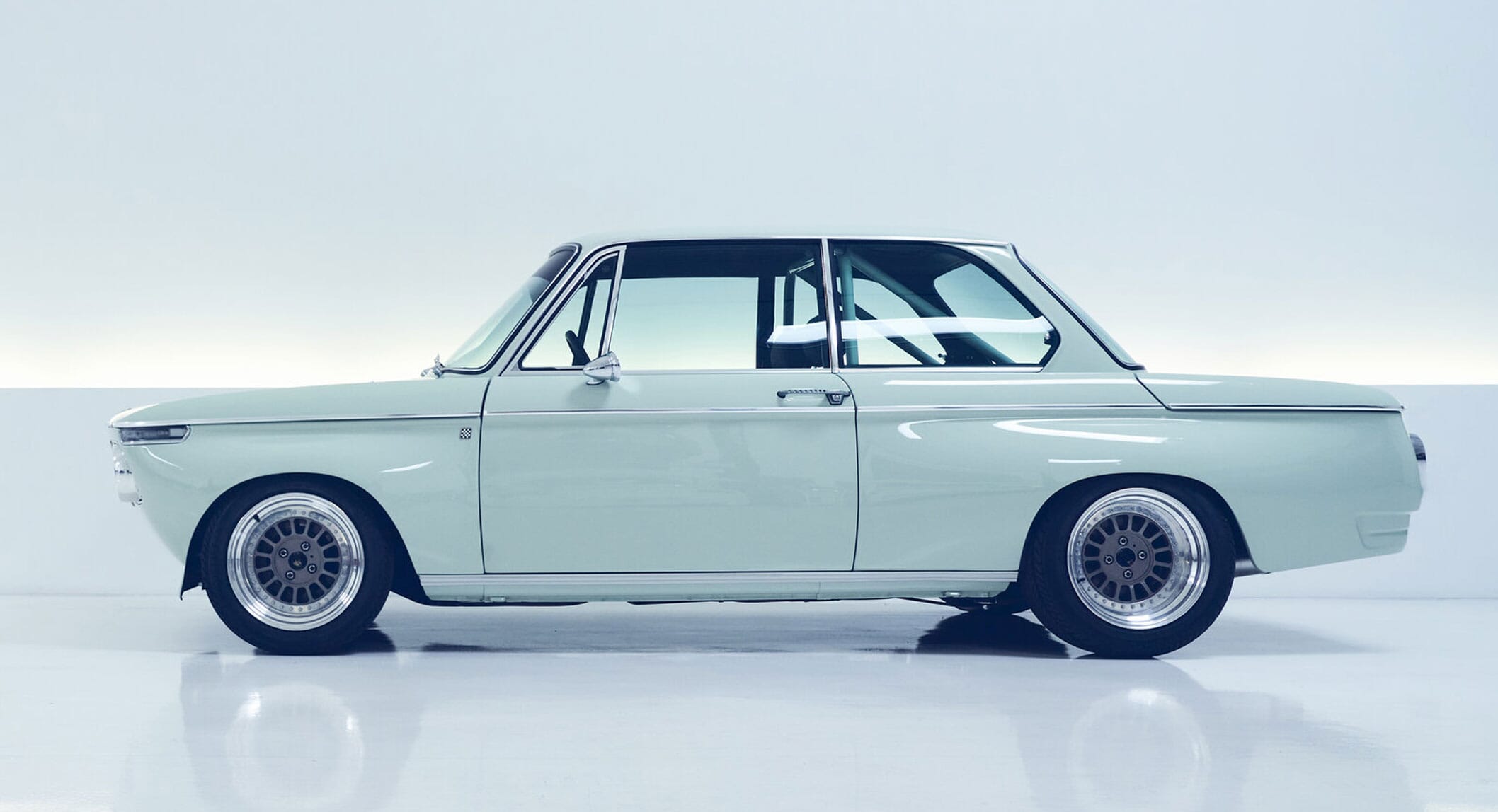 Light green vintage BMW 2002 with custom alloy wheels in a minimalist studio setting.