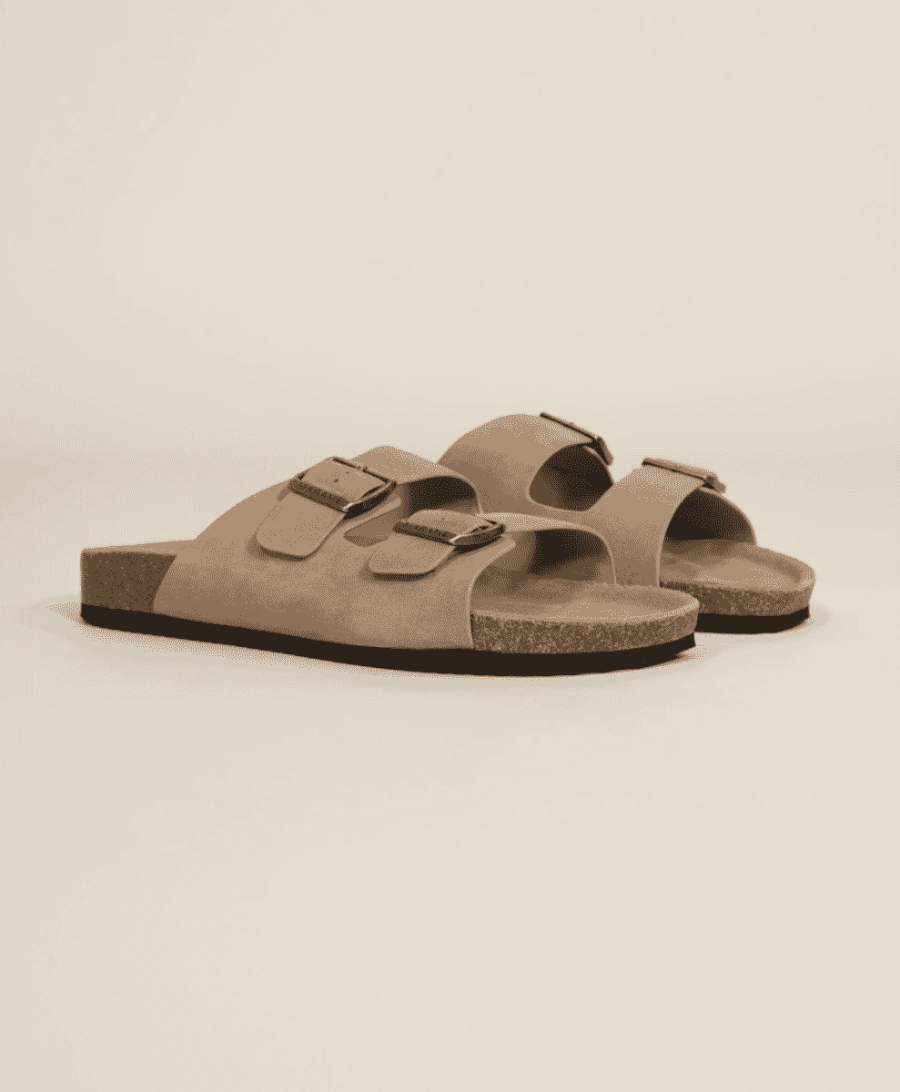 Studio product shot of beige suede sandals with cork soles and metal buckles