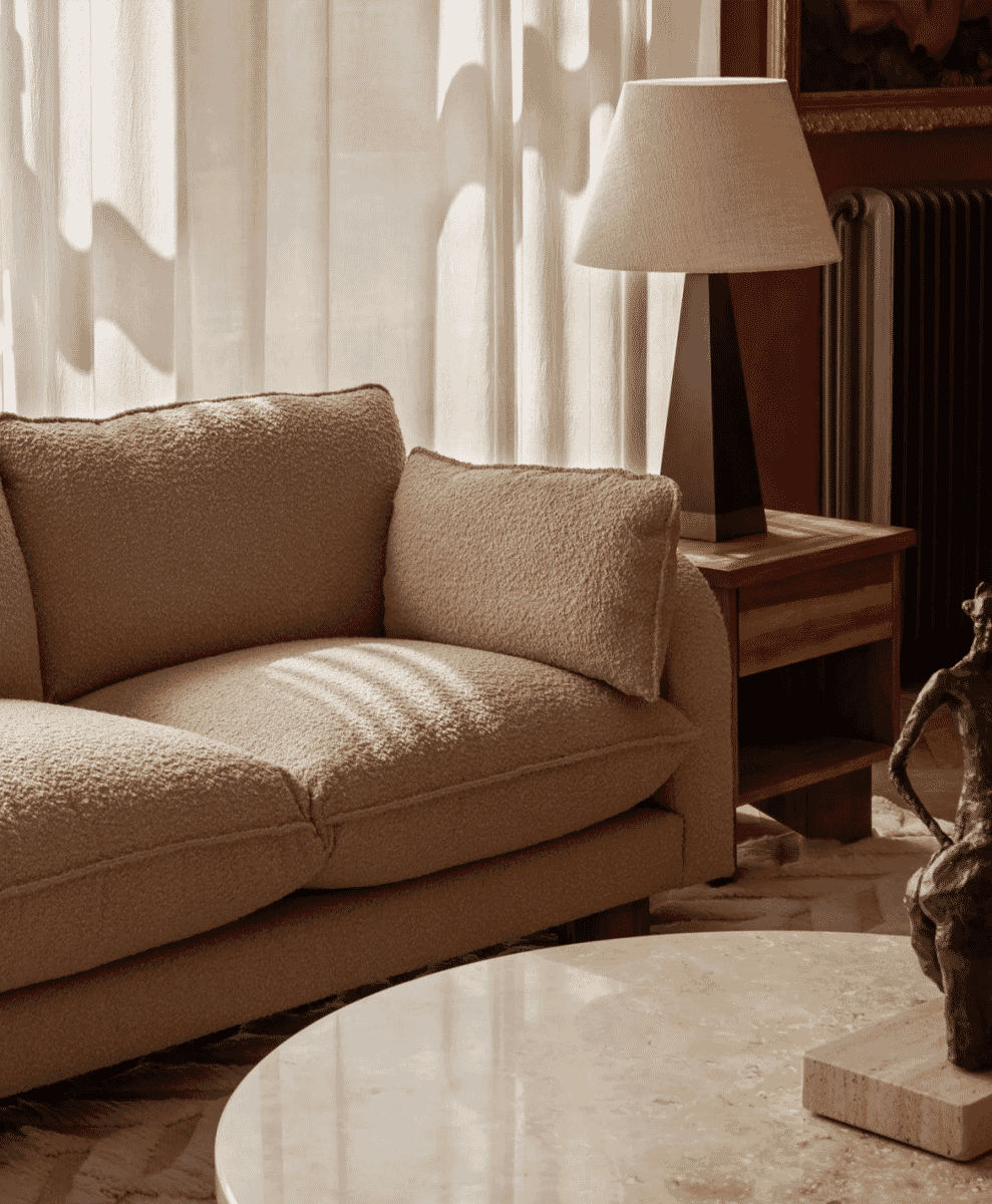 Beige bouclé sofa in a sunlit minimalist room with sheer curtains.