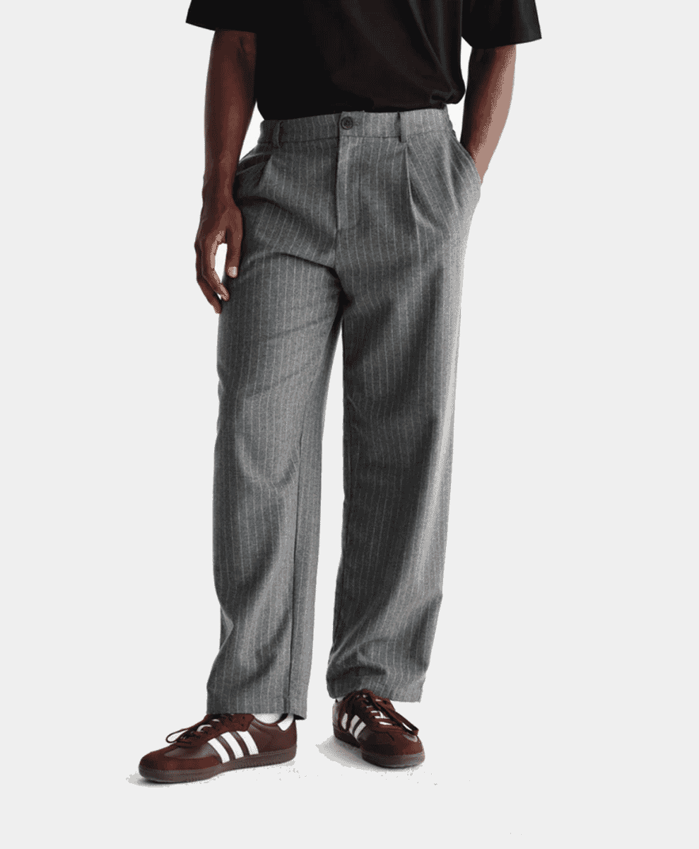Man wearing grey pinstripe pleated trousers with brown sneakers.