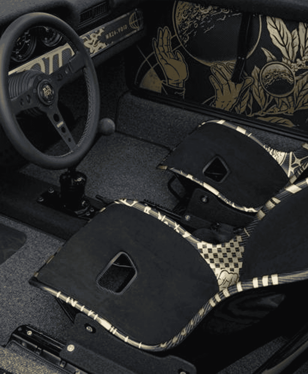 Custom car interior with black racing seats featuring gold and white patterns.